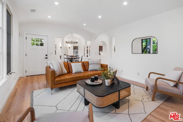 living room featuring an inviting chandelier, lofted ceiling, and light hardwood / wood-style flooring