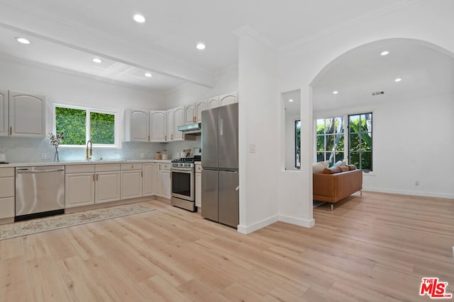 kitchen featuring light wood-type flooring, ornamental molding, appliances with stainless steel finishes, beamed ceiling, and decorative backsplash