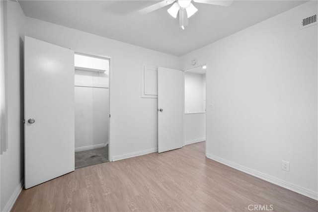 unfurnished bedroom featuring ceiling fan, light hardwood / wood-style floors, a closet, and a walk in closet