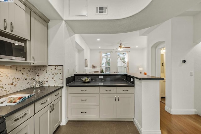 kitchen with dark wood-type flooring, ceiling fan, kitchen peninsula, and decorative backsplash