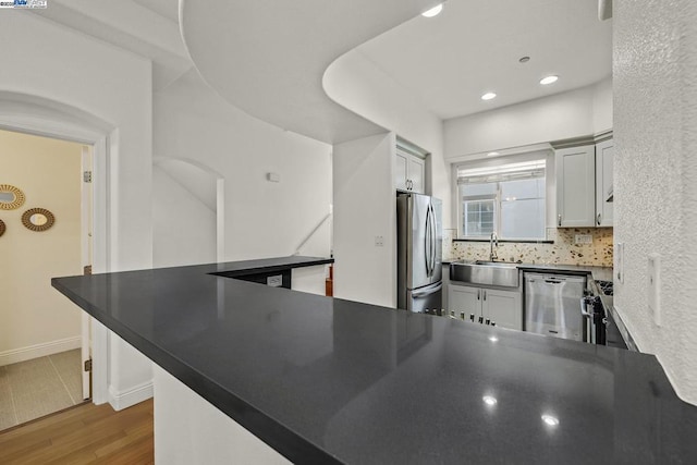 kitchen with sink, appliances with stainless steel finishes, backsplash, hardwood / wood-style floors, and kitchen peninsula