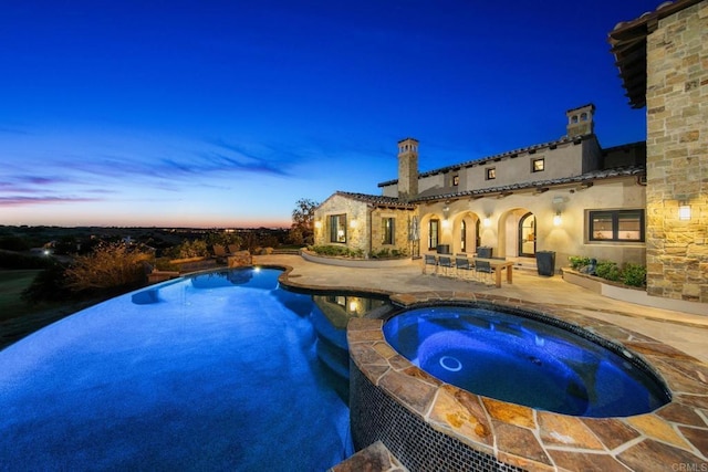 pool at dusk featuring a patio area and an in ground hot tub