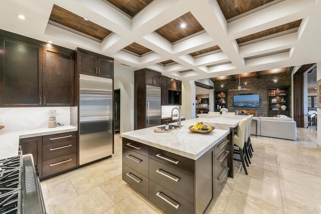 kitchen with sink, a breakfast bar, appliances with stainless steel finishes, coffered ceiling, and an island with sink