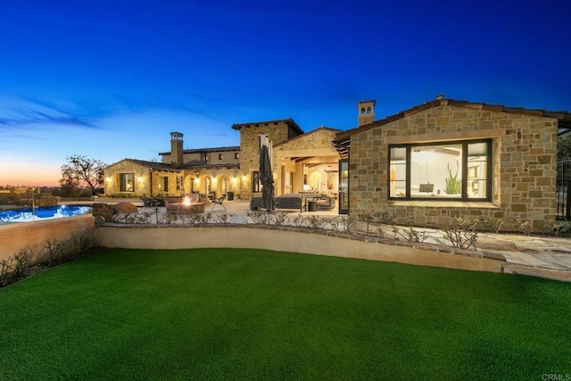 back house at dusk with a patio, a swimming pool, and a lawn