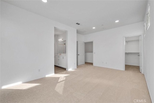 unfurnished bedroom featuring ensuite bathroom, a walk in closet, light carpet, and a closet