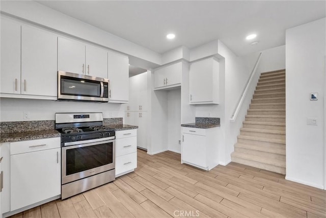 kitchen with white cabinetry, appliances with stainless steel finishes, light hardwood / wood-style floors, and dark stone countertops