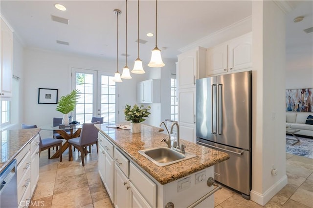 kitchen with pendant lighting, white cabinetry, sink, stainless steel appliances, and a center island with sink