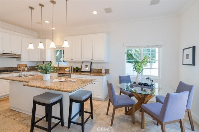 kitchen featuring crown molding, a kitchen island with sink, white cabinets, and light stone counters