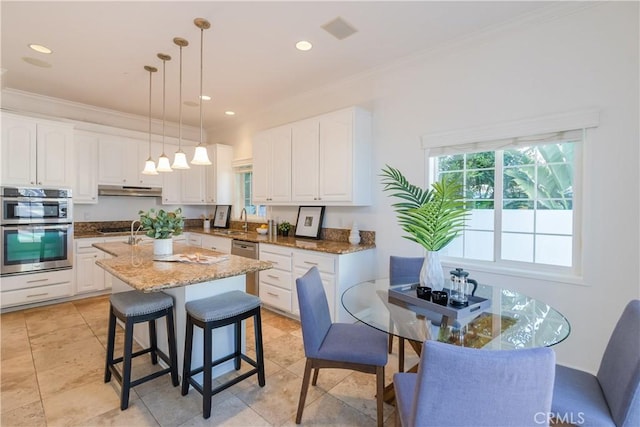 kitchen with white cabinetry, stone countertops, pendant lighting, stainless steel double oven, and a kitchen island with sink