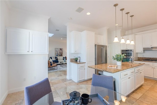 kitchen featuring hanging light fixtures, light stone countertops, an island with sink, and white cabinets