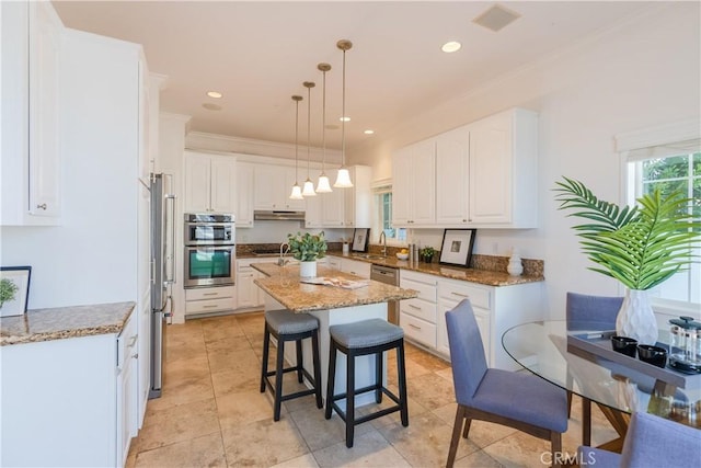 kitchen with pendant lighting, light stone countertops, white cabinets, and a center island with sink