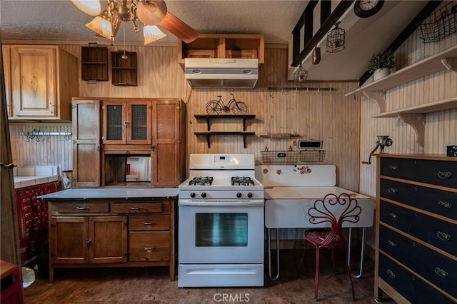 kitchen with ceiling fan, wooden walls, white gas range oven, and a textured ceiling