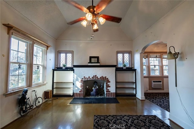 unfurnished living room featuring radiator heating unit, vaulted ceiling, a wealth of natural light, and a wall mounted air conditioner