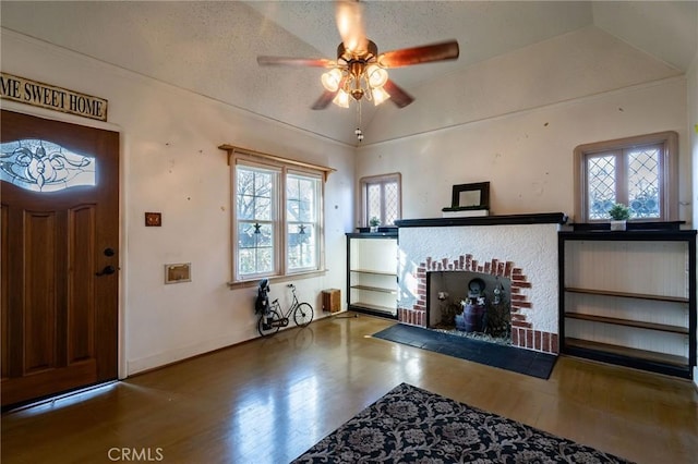 foyer with a fireplace, wood-type flooring, lofted ceiling, ceiling fan, and a textured ceiling