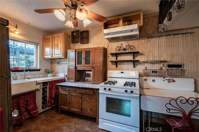 kitchen featuring white range with gas cooktop, tile counters, wooden walls, and a textured ceiling