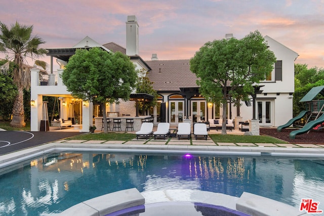 pool at dusk with french doors, exterior bar, and a patio area