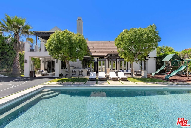 view of swimming pool with a patio area, a playground, and exterior bar