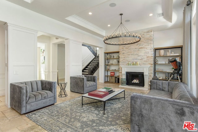 living room featuring an inviting chandelier, a large fireplace, ornamental molding, and a raised ceiling