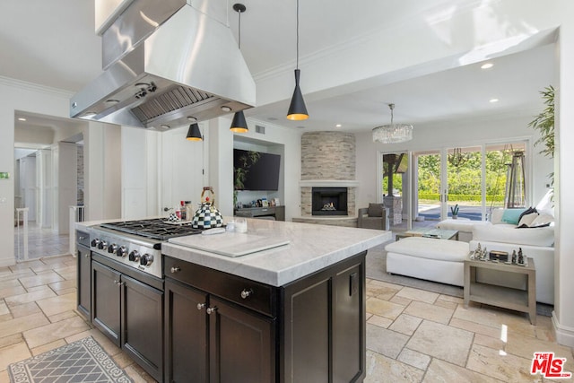 kitchen featuring a stone fireplace, island range hood, hanging light fixtures, ornamental molding, and a center island