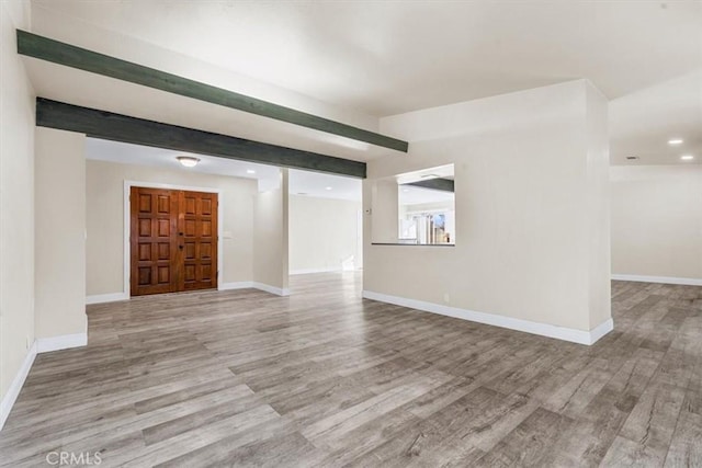 unfurnished living room featuring beamed ceiling and light hardwood / wood-style flooring