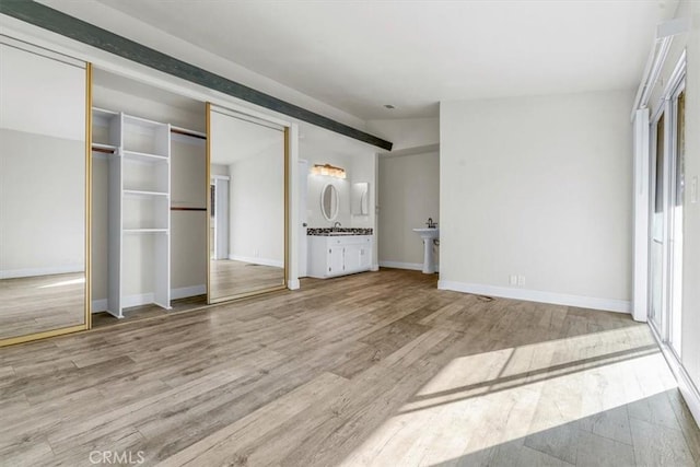 unfurnished bedroom with hardwood / wood-style flooring, sink, multiple closets, and ensuite bath