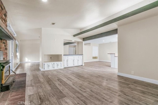 unfurnished living room with hardwood / wood-style flooring, a wood stove, and beam ceiling