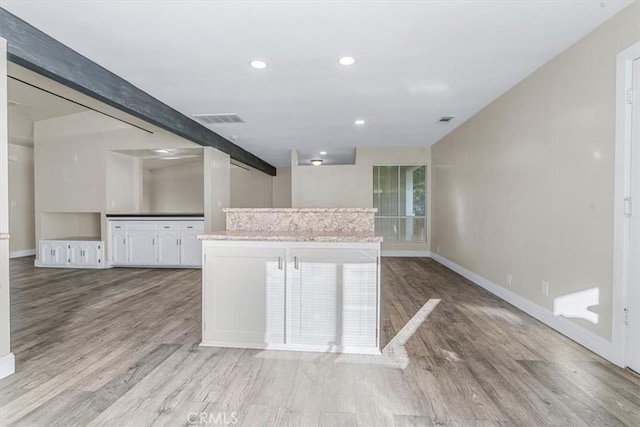 kitchen with light stone counters, beam ceiling, light hardwood / wood-style floors, and white cabinets