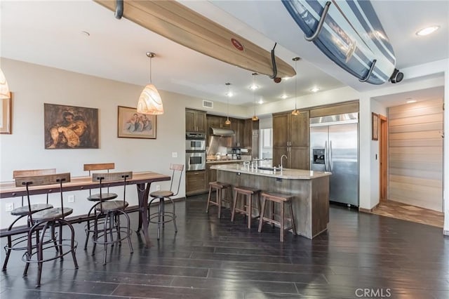 kitchen with dark brown cabinetry, a center island with sink, a kitchen breakfast bar, pendant lighting, and stainless steel appliances