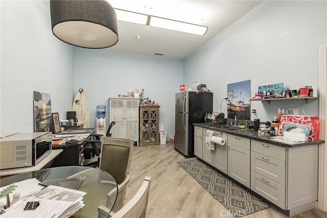 kitchen featuring sink, light hardwood / wood-style flooring, gray cabinets, stainless steel refrigerator, and dark stone countertops