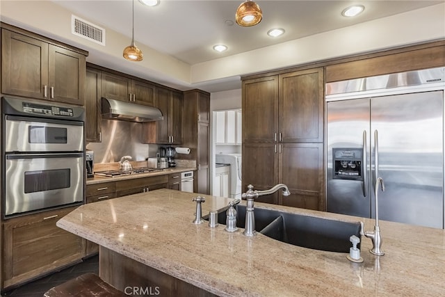 kitchen with pendant lighting, sink, dark brown cabinetry, stainless steel appliances, and light stone countertops