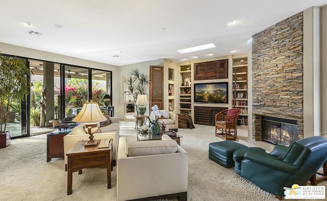 carpeted living room featuring a stone fireplace and a skylight