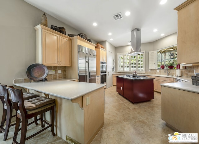 kitchen featuring stainless steel appliances, island exhaust hood, light brown cabinets, and kitchen peninsula