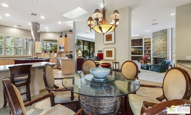 dining area with a chandelier, a stone fireplace, and a skylight