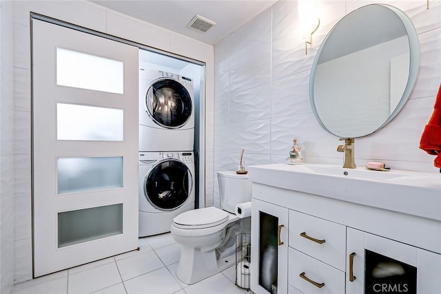 bathroom featuring tile walls, stacked washer and dryer, vanity, toilet, and tile patterned floors