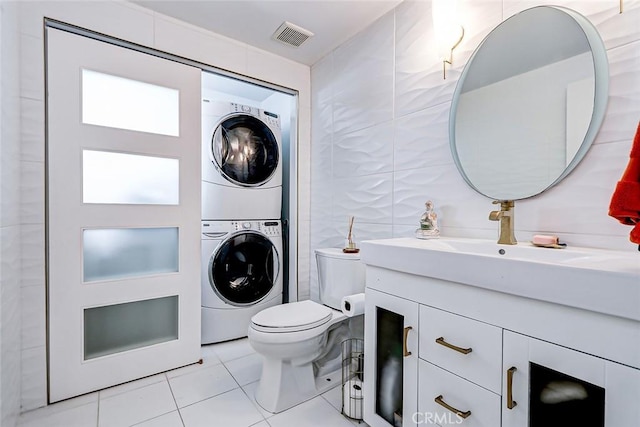 bathroom with stacked washer / dryer, visible vents, toilet, tile walls, and tile patterned flooring