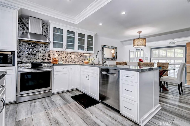 kitchen with white cabinets, appliances with stainless steel finishes, decorative light fixtures, and wall chimney range hood