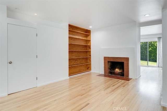 unfurnished living room with a fireplace, built in features, and light wood-type flooring