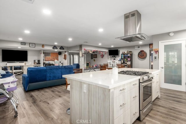 kitchen with stainless steel range with gas cooktop, island exhaust hood, light hardwood / wood-style floors, and a kitchen island