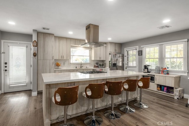 kitchen featuring sink, stainless steel appliances, a center island, island exhaust hood, and decorative backsplash