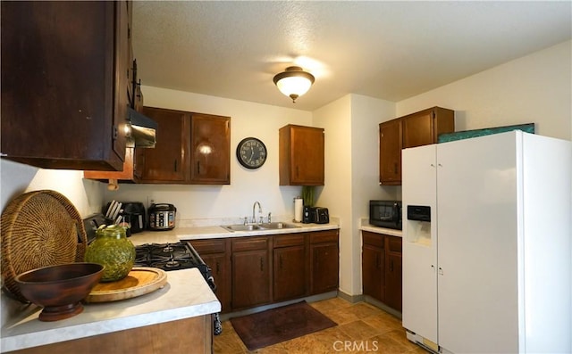 kitchen with dark brown cabinets, sink, and white fridge with ice dispenser