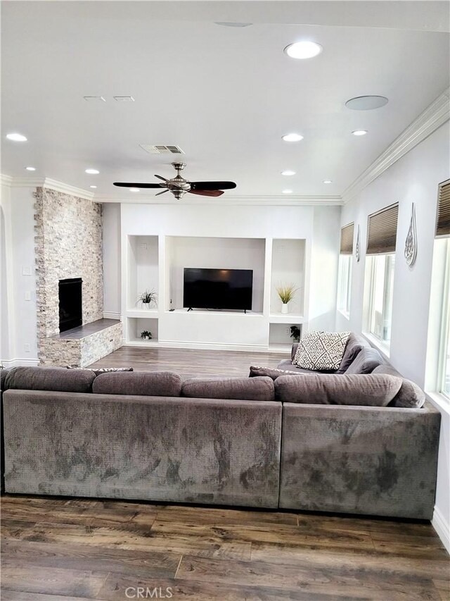 living room featuring crown molding, dark hardwood / wood-style floors, a stone fireplace, and ceiling fan