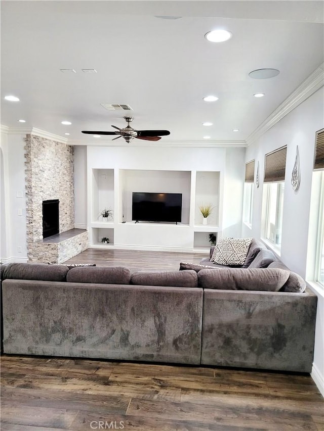 living area with dark wood-style floors, visible vents, crown molding, and a stone fireplace