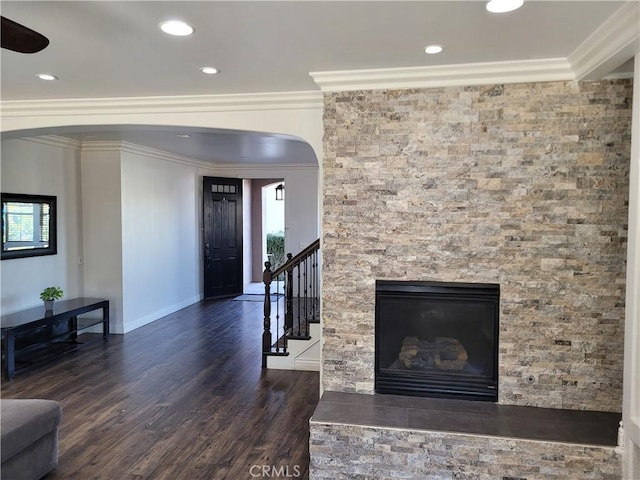 living room with arched walkways, dark wood-type flooring, stairs, a glass covered fireplace, and crown molding