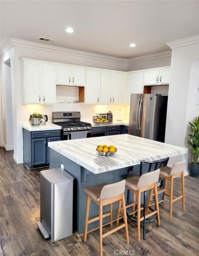 kitchen with blue cabinets, white cabinetry, a kitchen breakfast bar, appliances with stainless steel finishes, and ornamental molding