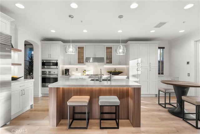 kitchen with an island with sink, appliances with stainless steel finishes, white cabinetry, and decorative light fixtures