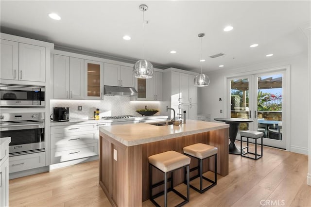 kitchen with an island with sink, stainless steel appliances, hanging light fixtures, sink, and decorative backsplash