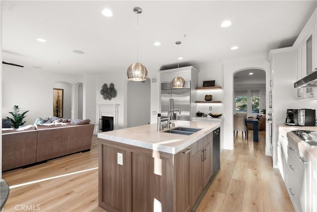 kitchen with stainless steel built in fridge, decorative light fixtures, sink, white cabinetry, and a kitchen island with sink