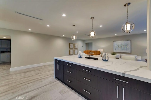 kitchen with light stone countertops, sink, pendant lighting, and light hardwood / wood-style floors