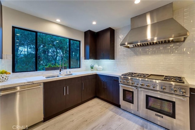 kitchen with sink, dark brown cabinets, range hood, stainless steel appliances, and light hardwood / wood-style floors