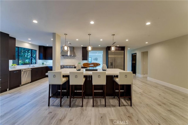 kitchen featuring hanging light fixtures, appliances with stainless steel finishes, wall chimney exhaust hood, and a spacious island